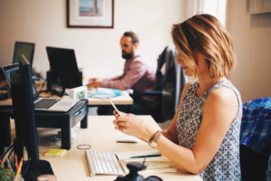 Women sitting at computer looking at phone